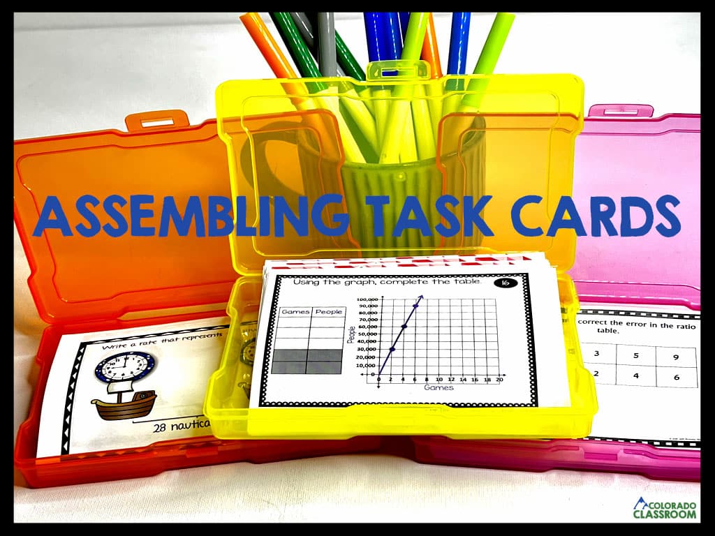 Three colorful task card boxes are stacked in a pyramid formation on top of each other, open, and with task cards inside them. In the back is a coffee mug with markers.