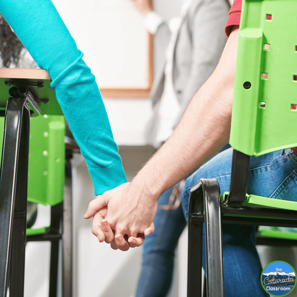 This image shows two students holding hands in class. This behavior can be lessened if the teacher uses proximity.