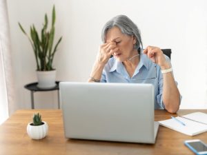Tired and overworked stressed mature woman working on laptop at home indoor, female teacher feeling exhausted after lecturing students online, touching eyes. Smart working senior people and technology